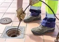 Plumber using motorized drain snake cable machine to clear interior drain blockage