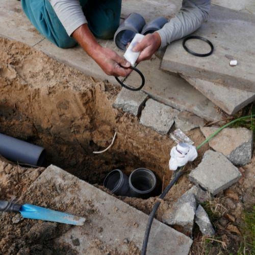 Plumbing technician fitting and inspecting sewer line connection joint in excavated trench
